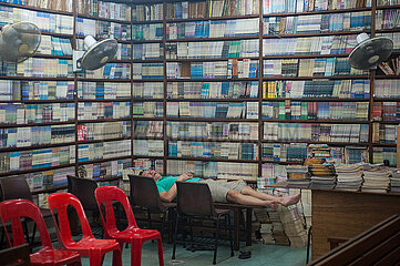 Singapur  Republik Singapur  Ein Buchhaendler schlaeft auf einem Tisch in einem Buchladen in Chinatown