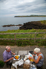 Grossbritannien  Nordirland  Portballintrae  County Antrim - Glueckliches Rentnerpaar bei Fish and chips mit Blick auf die Irische See