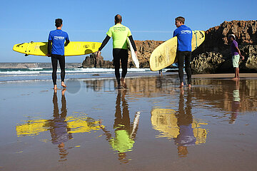 Raposeira  Portugal  Menschen tragen bei einem Surfkurs ihre Surfbretter ins Wasser