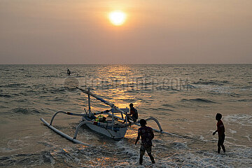Senggigi  Indonesien  Maenner haben ein Jukung bei Sonnenuntergang ins Meer geschoben. Ein Jukung ist ein traditionelles indonesisches Fischerboot