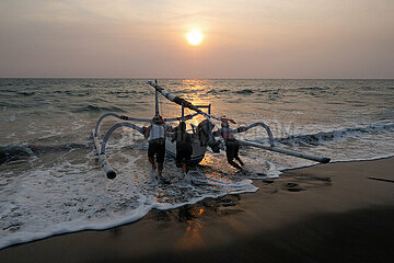 Senggigi  Indonesien  Maenner schieben ein Jukung bei Sonnenuntergang ins Meer. Ein Jukung ist ein traditionelles indonesisches Fischerboot