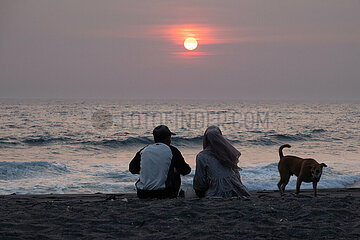 Senggigi  Indonesien  Mann und Frau sitzen bei Sonnenuntergang mit ihrem Hund am Strand