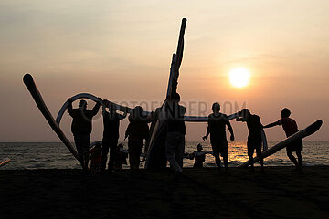 Senggigi  Indonesien  Silhouette: Maenner schieben ein Jukung bei Sonnenuntergang ins Meer. Ein Jukung ist ein traditionelles indonesisches Fischerboot