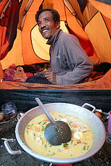 Senaru  Indonesien  Mann sitzt in einem Zelt vor einer Schuessel mit frisch gekochter Suppe