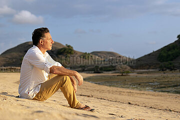 Kuta  Indonesien  Mann sitzt am Strand und sonnt sich