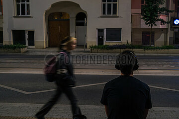Polen  Poznan - junger Mann mit Kopfhoerern wartet an einer Strassenbahnhaltestelle  ein Maedchen laeuft vorbei