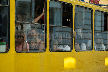 Ukraine  Lwiw - Ukrainekrieg: Ernst schauende Fahrgaeste einer Strassenbahn  die fuer einen Beerdigungszug fuer zwei gefallene ukrainische Soldaten angehalten wurde