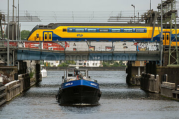 Niederlande  Amsterdam - Zug der Niederlaendische Eisenbahnen AG ueberquert Bruecke ueber das IJ im Stadtzentrum  unten faehrt ein Schiff