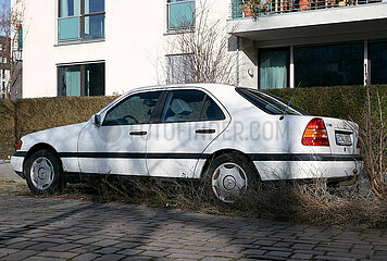 Berlin  Deutschland - Parkender weisse Mercedes Limousine am Strassenrand waechst allmaehlich mit Gras und Baumtrieben zu.