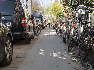 Konfliktzone Gehweg – Fußgänger zwischen parkenden Autos und abgestellten Fahrrädern