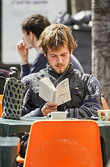 junger Mann liest ein Buch im Straßencafé