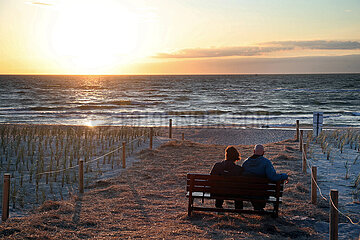 Dierhagen  Deutschland  Paerchen sitzt am Strand der Ostsee bei Sonnenuntergang auf einer Bank