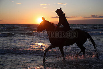 Dierhagen  Silhouette: Frau reitet bei Sonnenuntergang auf ihrem Pferd am Strand der Ostsee