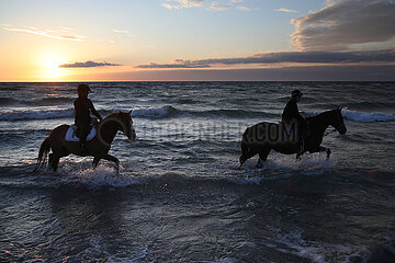 Dierhagen  Silhouette: Frauen reiten bei Sonnenuntergang auf ihren Pferden durch das Wasser der Ostsee