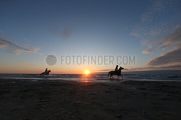 Dierhagen  Silhouette: Frauen reiten bei Sonnenuntergang auf ihren Pferden am Strand durch die Wellen der Ostsee