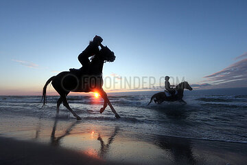 Dierhagen  Silhouette: Frauen reiten bei Sonnenuntergang auf ihren Pferden am Strand der Ostsee
